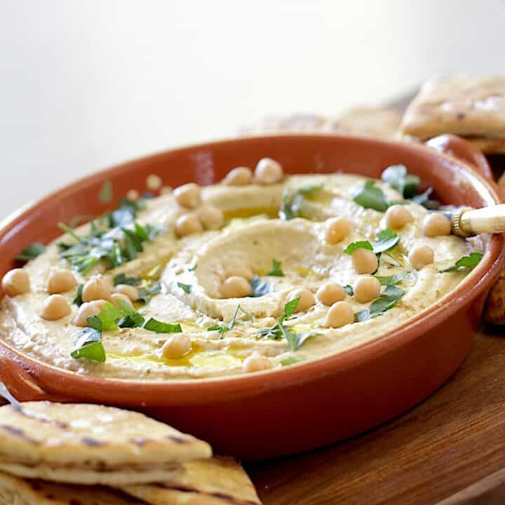 homemade hummus in a terra cotta dish on a board with pita