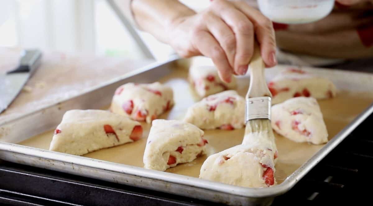 Brushing cream mixture on to cut scones on a baking sheet