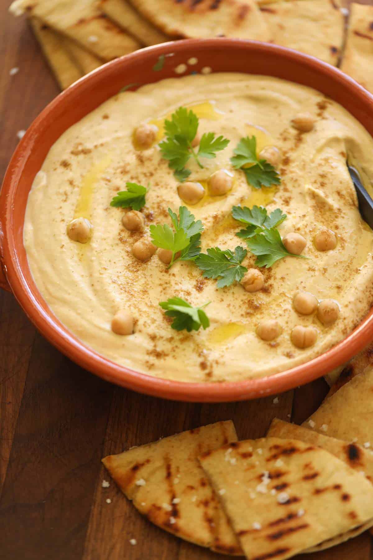 a terra cotta dish with hummus and pita