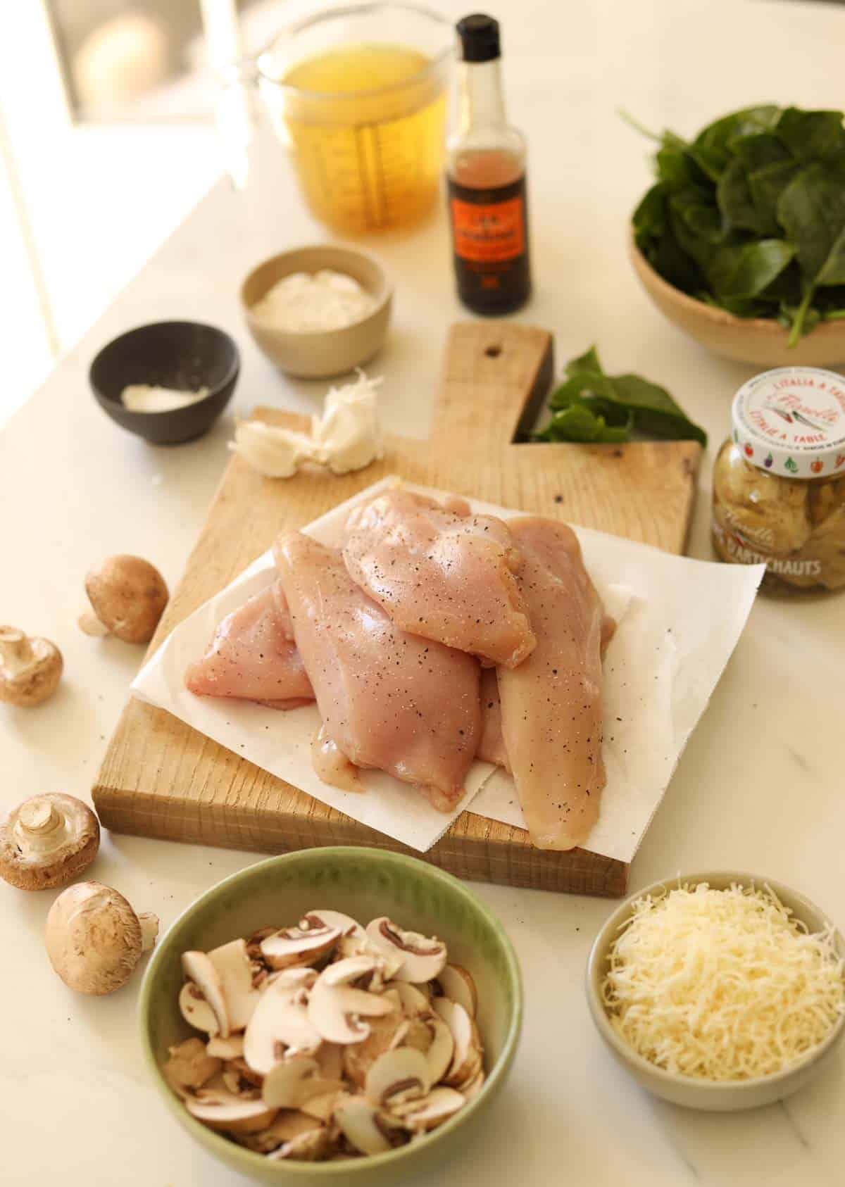 Chicken, spinach, arichokes, cheese, mushrooms, chicken broth and other ingredients on an counter.