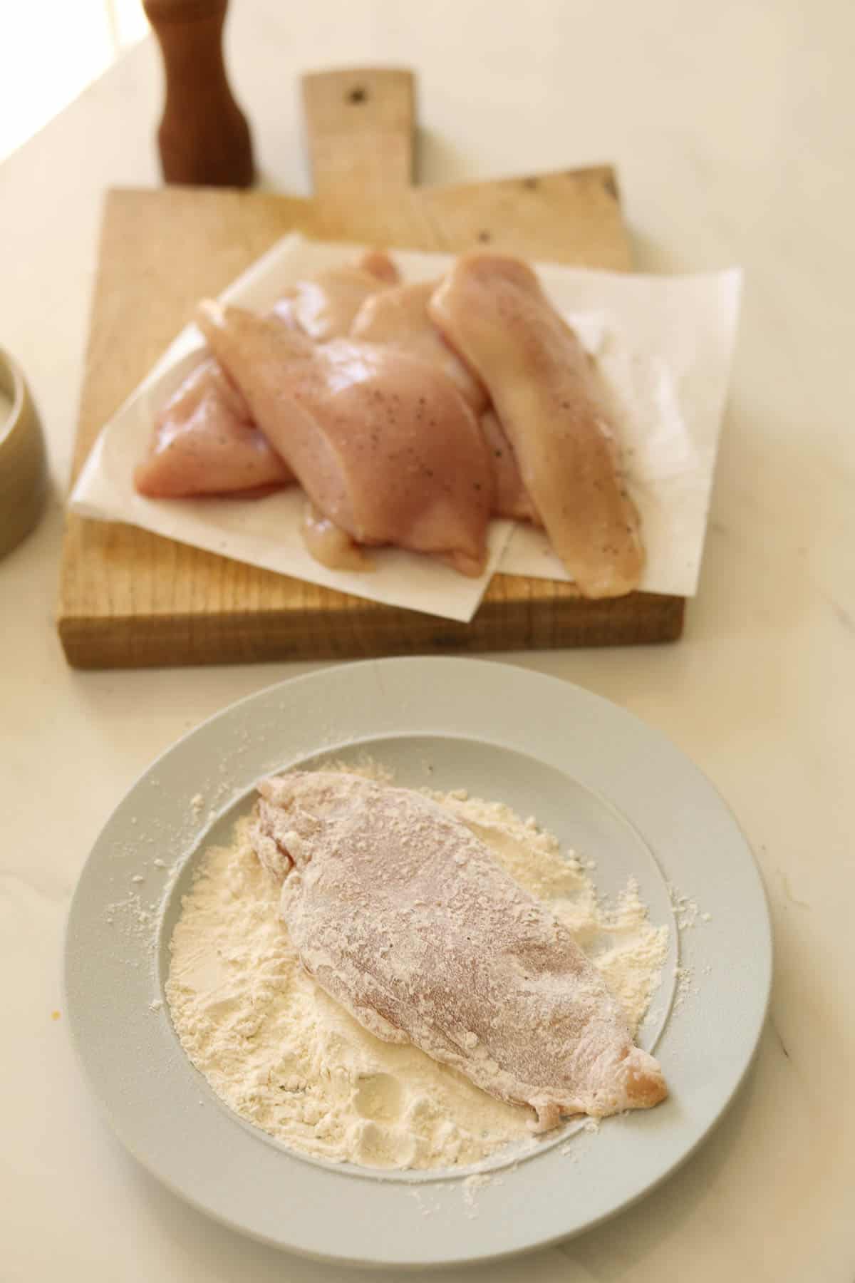 Chicken breasts being dusted with flour on a plate.