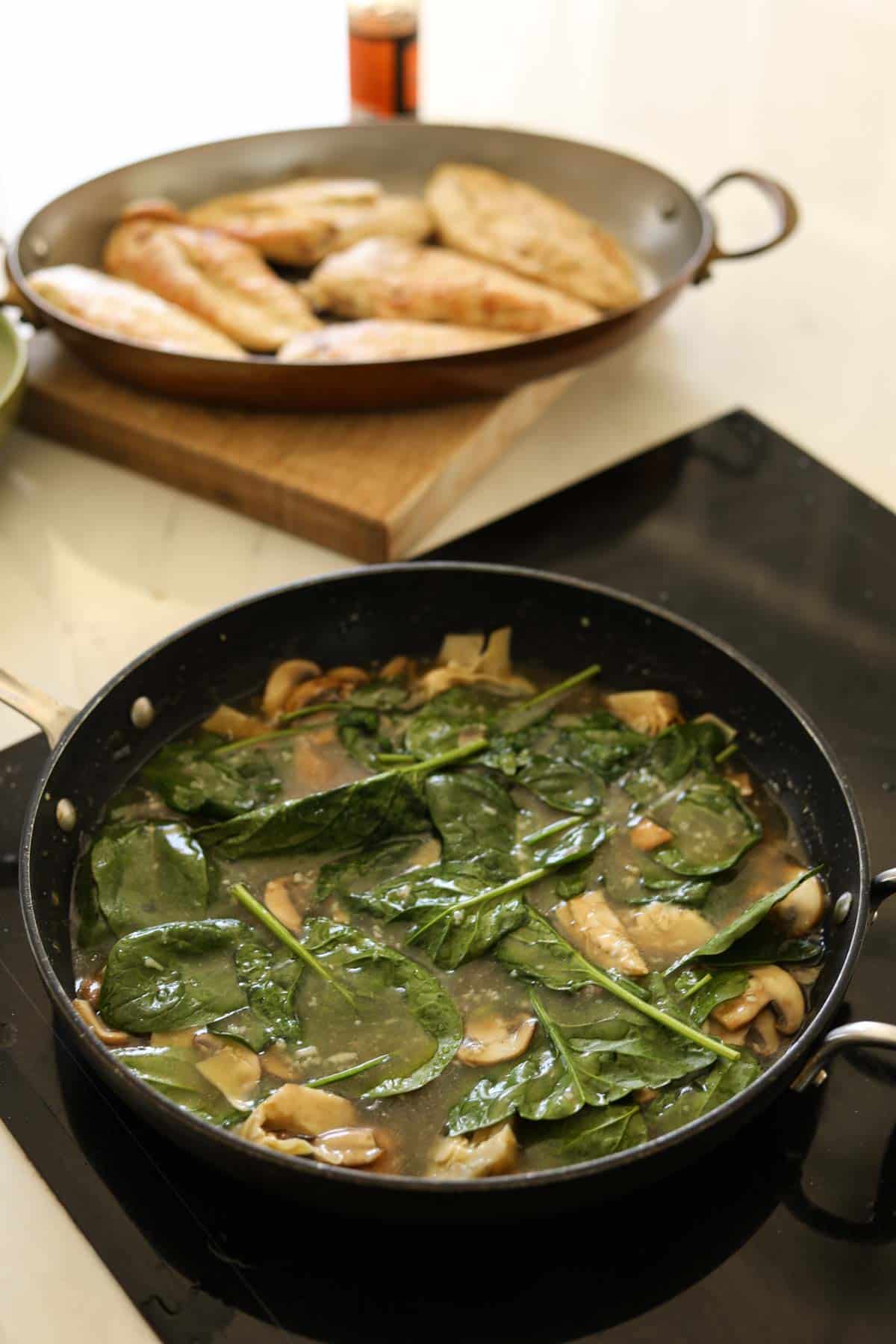 A skillet simmering with spinach, chicken, artichokes and chicken broth.
