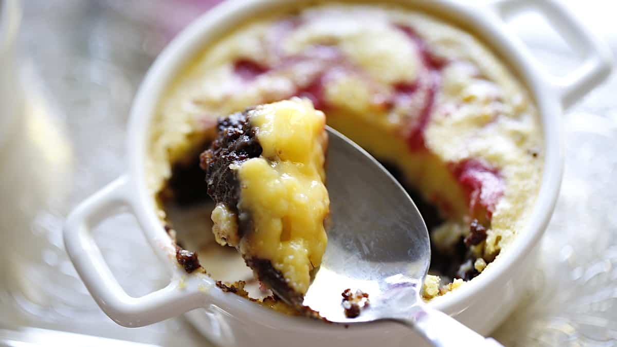 a spoon taking a bite of a lemon bar dessert with brownie bottom