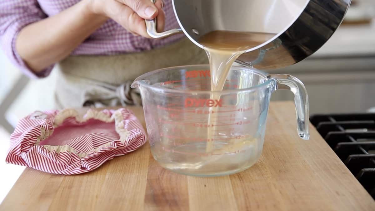 a person pouring grapefruit syrup from a pot into a pitcher