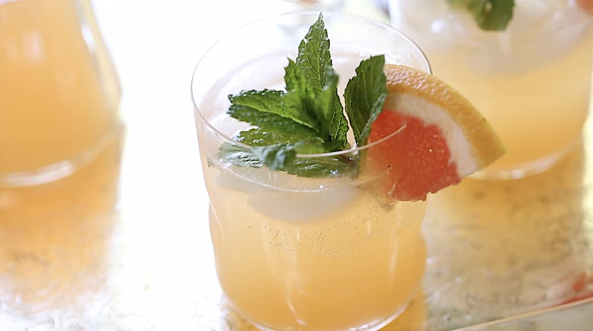 a small glass filled with grapefruit syrup and sparkling water garnished with mint and grapefruit