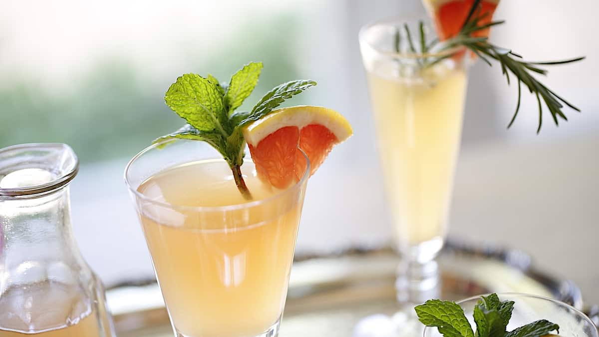 2 cocktails garnished with grapefruit, mint and rosemary on a silver tray