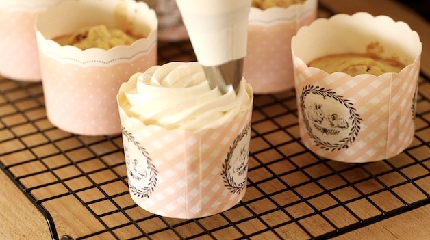 A tight shot of a pastry bag decorating a cupcake with frosting