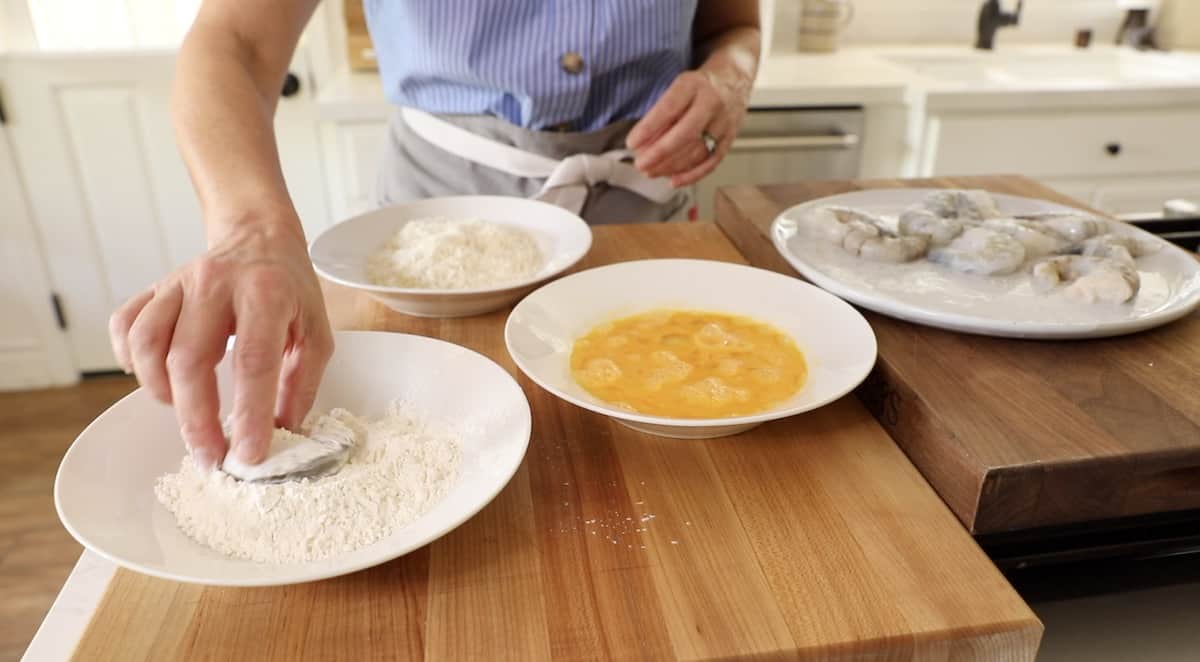 a person dipping a shrimp in a bowl of flour and dredging it