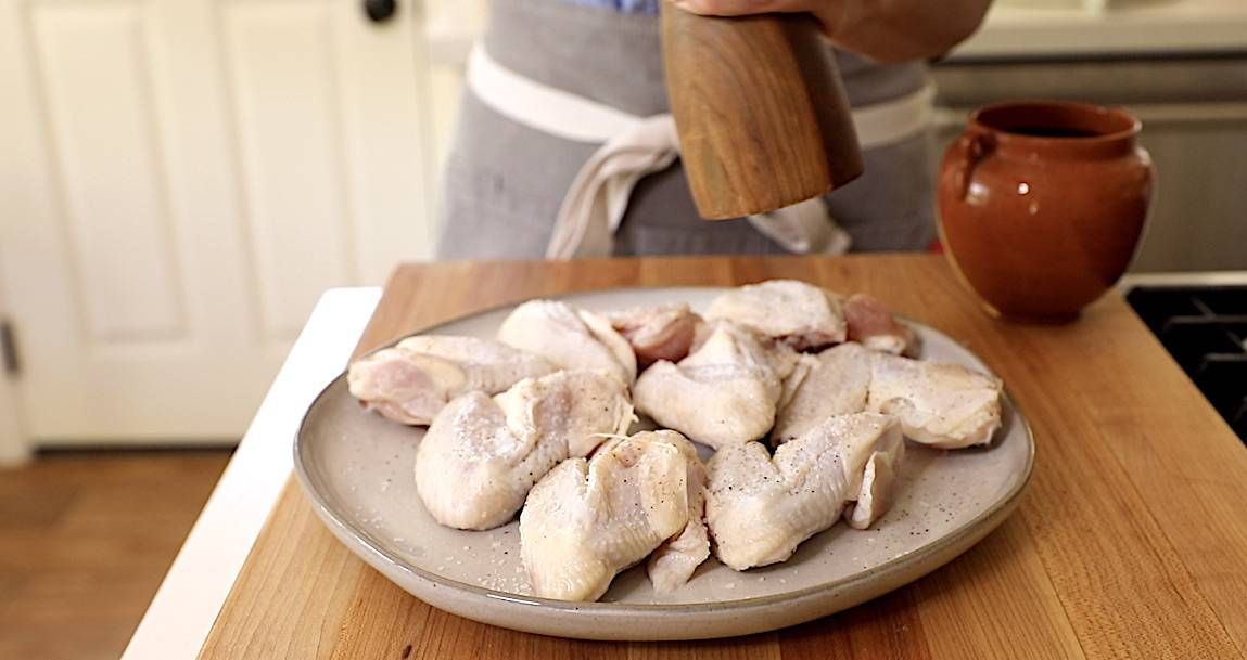 A person seasoning raw chicken wings
