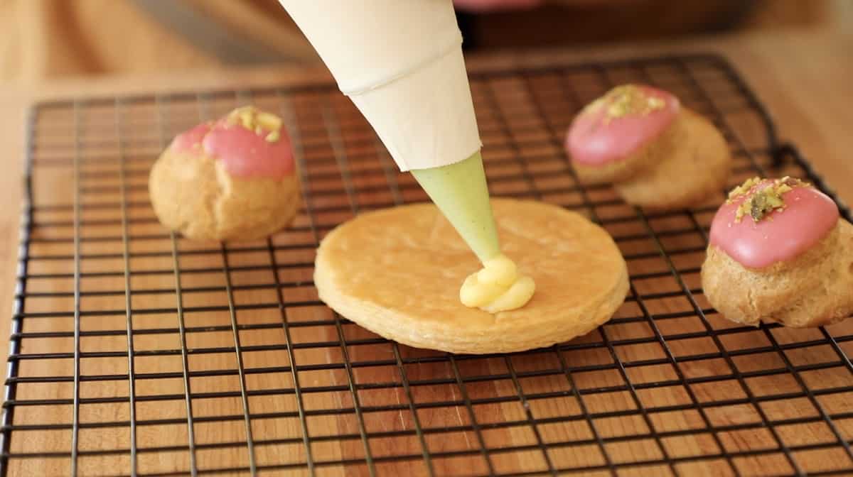 a person piping pastry cream on a puff pastry base