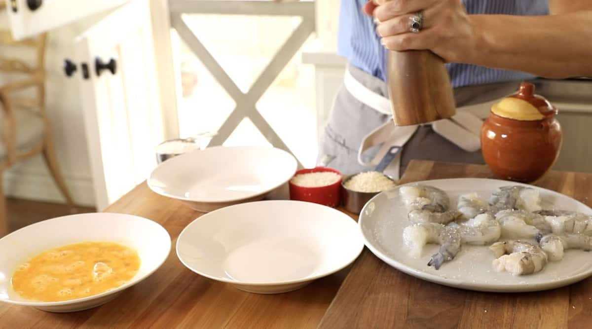 a person seasoning raw shrimp with pepper at a dredging station