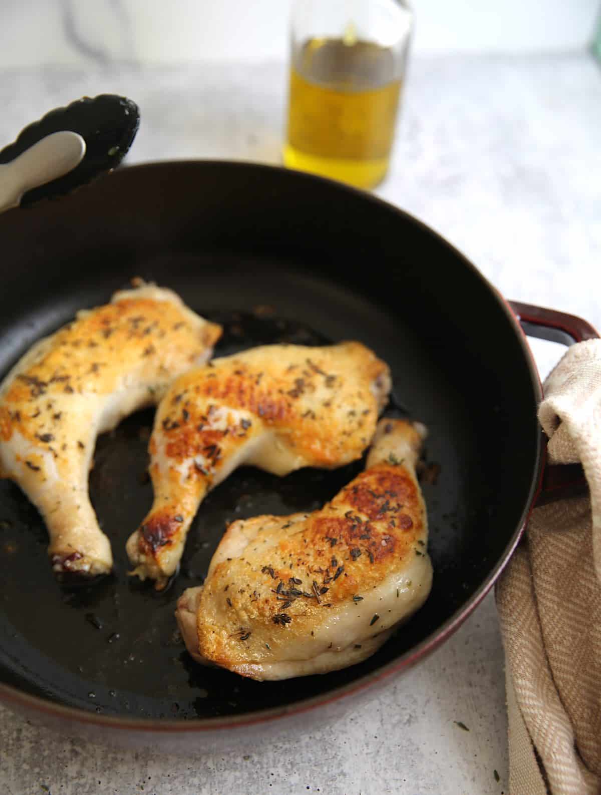 Chicken legs seared in a pan with olive oil in the background