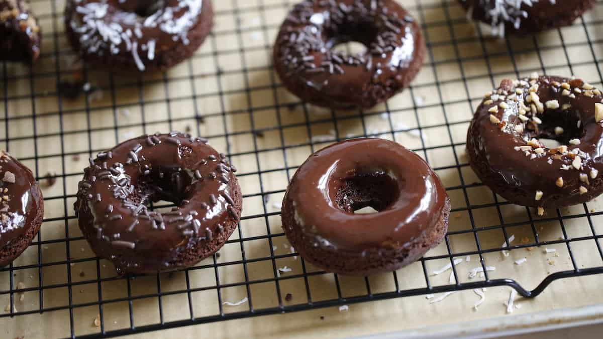 Chocolate donuts freshly glazed with ganache and toppings on a cooling rack