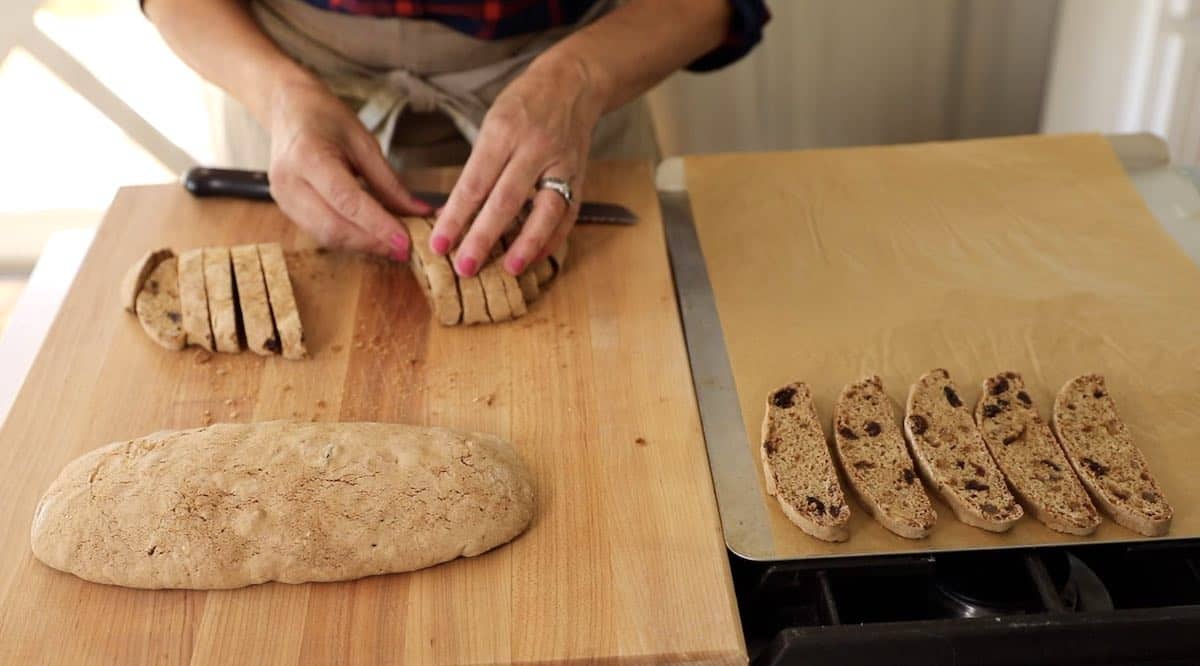 slicing biscotti cookies from a log and placing on a baking sheet