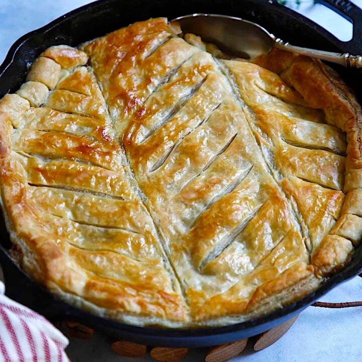 a chicken and mushroom pie in a cast iron skillet with a decorative puff pastry top