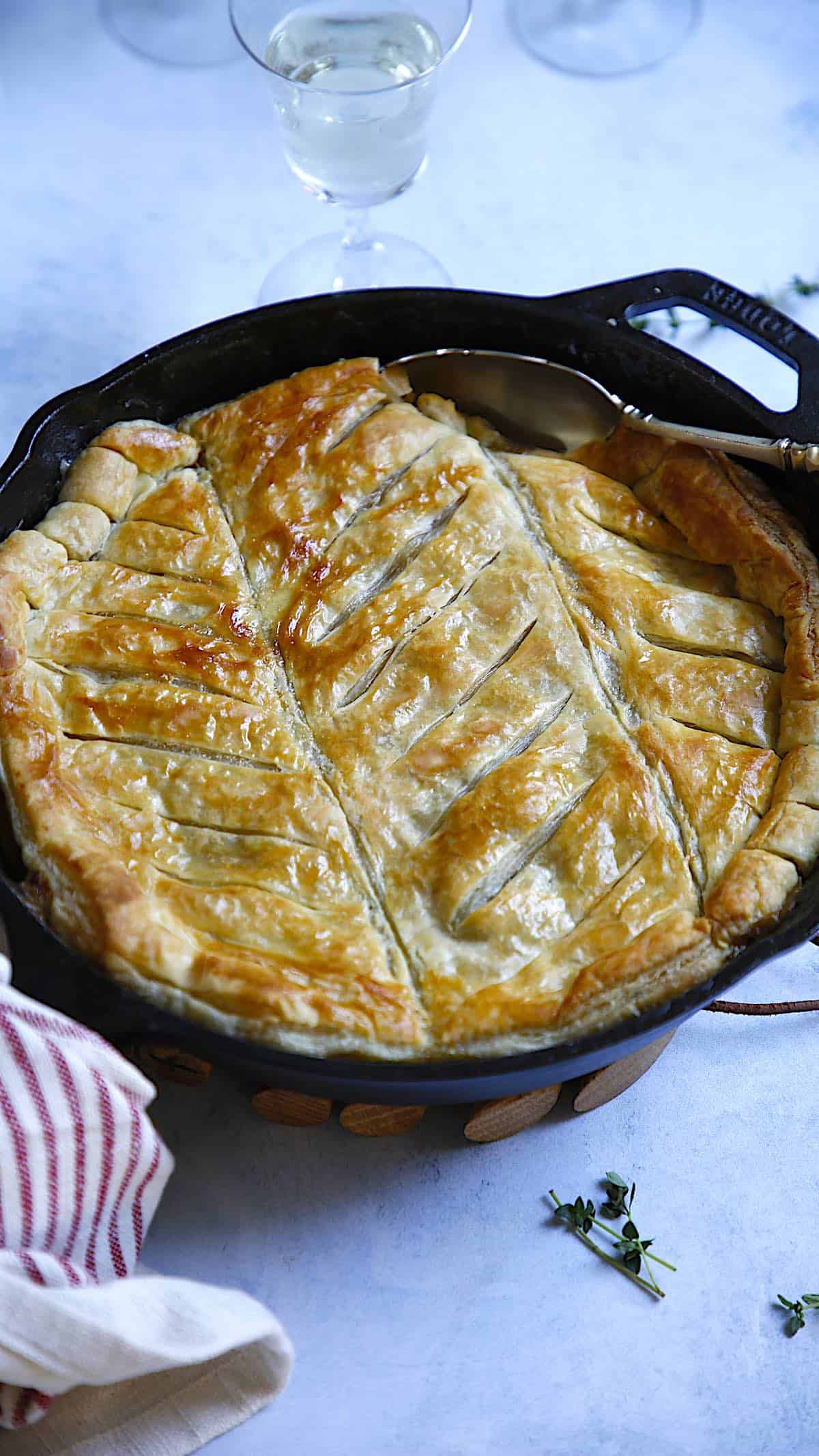 a chicken and mushroom pie in a cast iron skillet with a decorative puff pastry top
