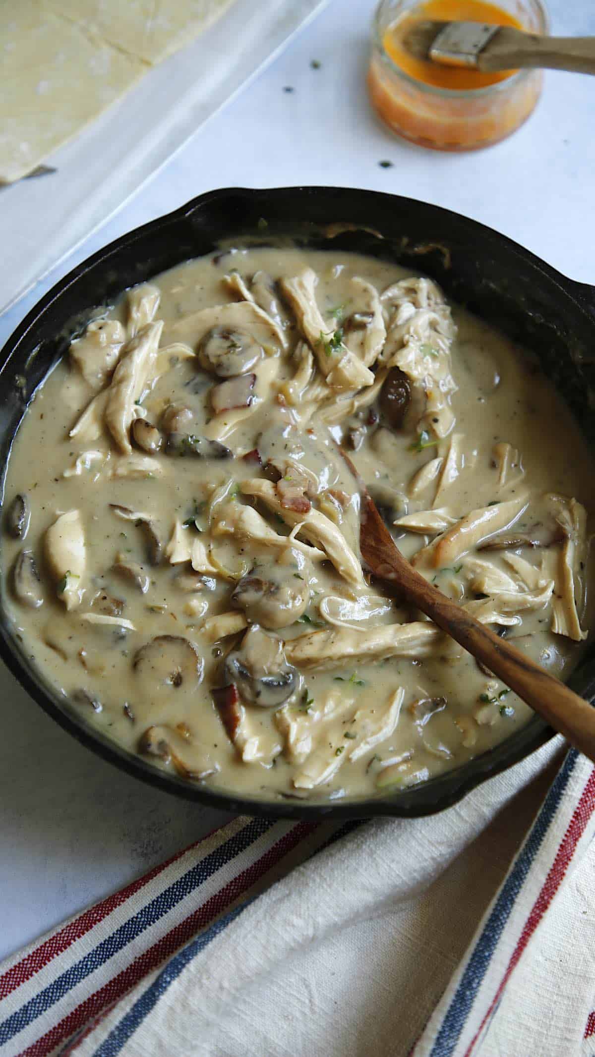 Chicken and mushrooms in a sauce in a cast ironb skillet with a wooden spoon