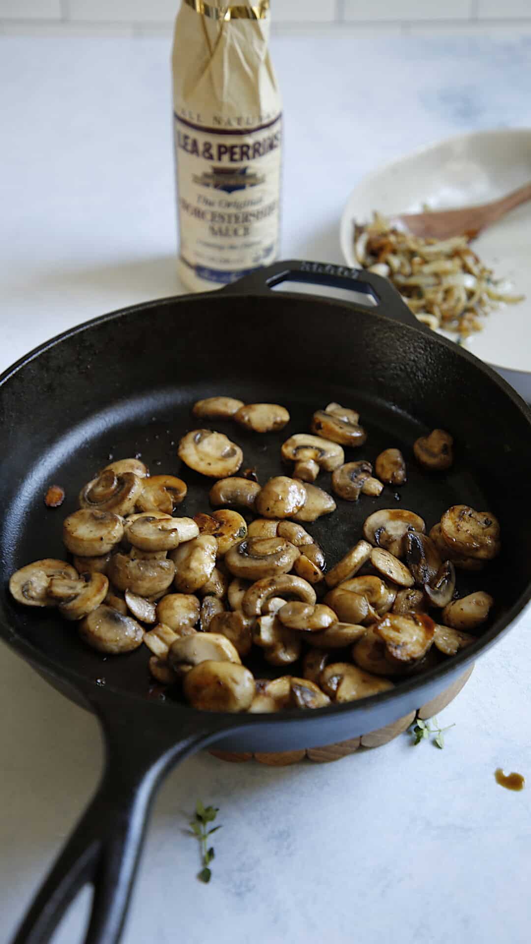 browned mushrooms in a cast iron skillet with Worcestershire sauce in background