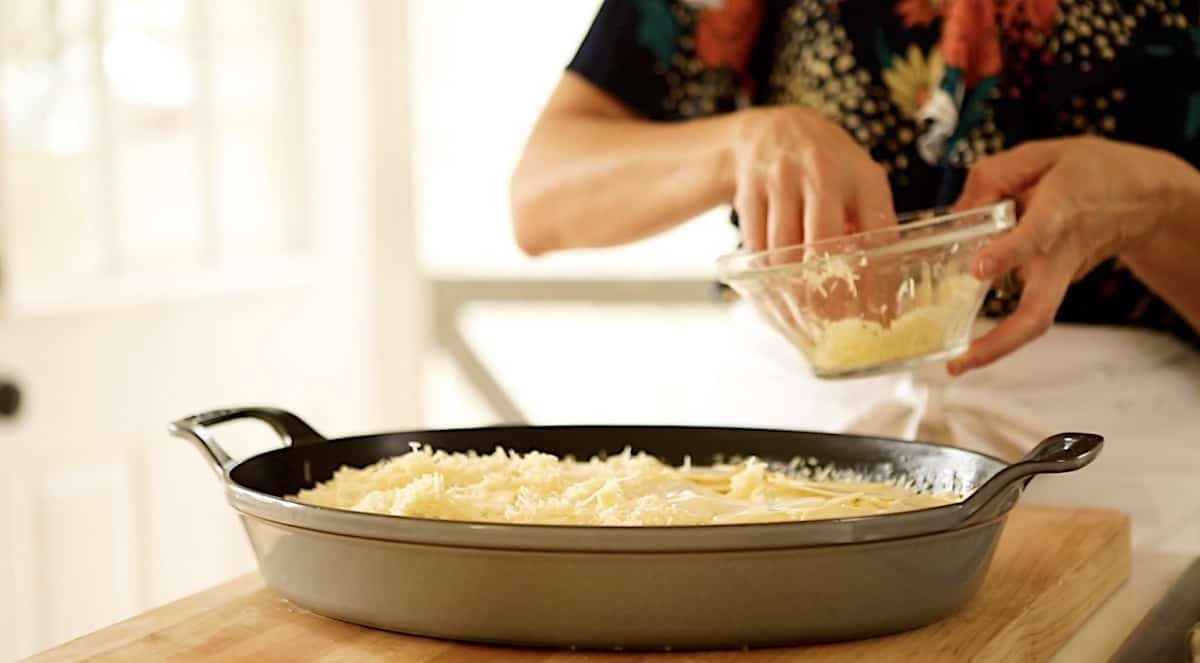 a person adding cheese to the top of a gratin dish
