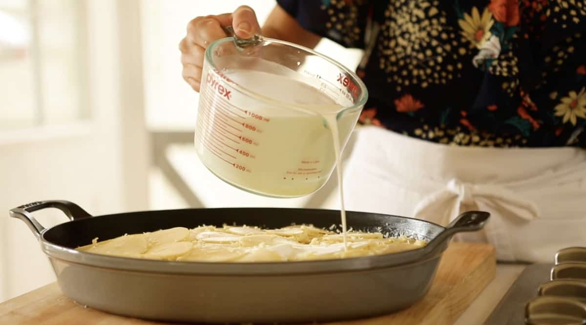 pouring milk and cream mixture on top of a potato casserole