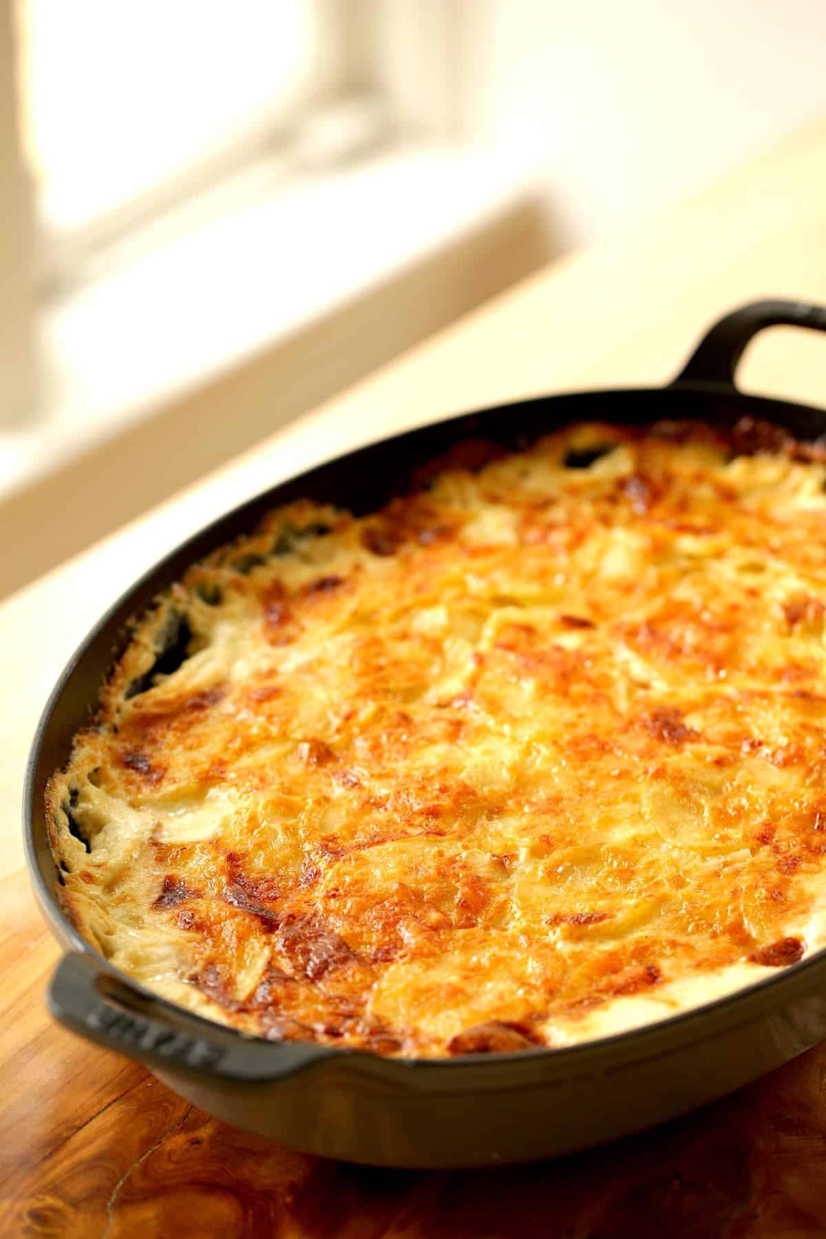 a vertical image of a gratin dish filled with potatoes au gratin