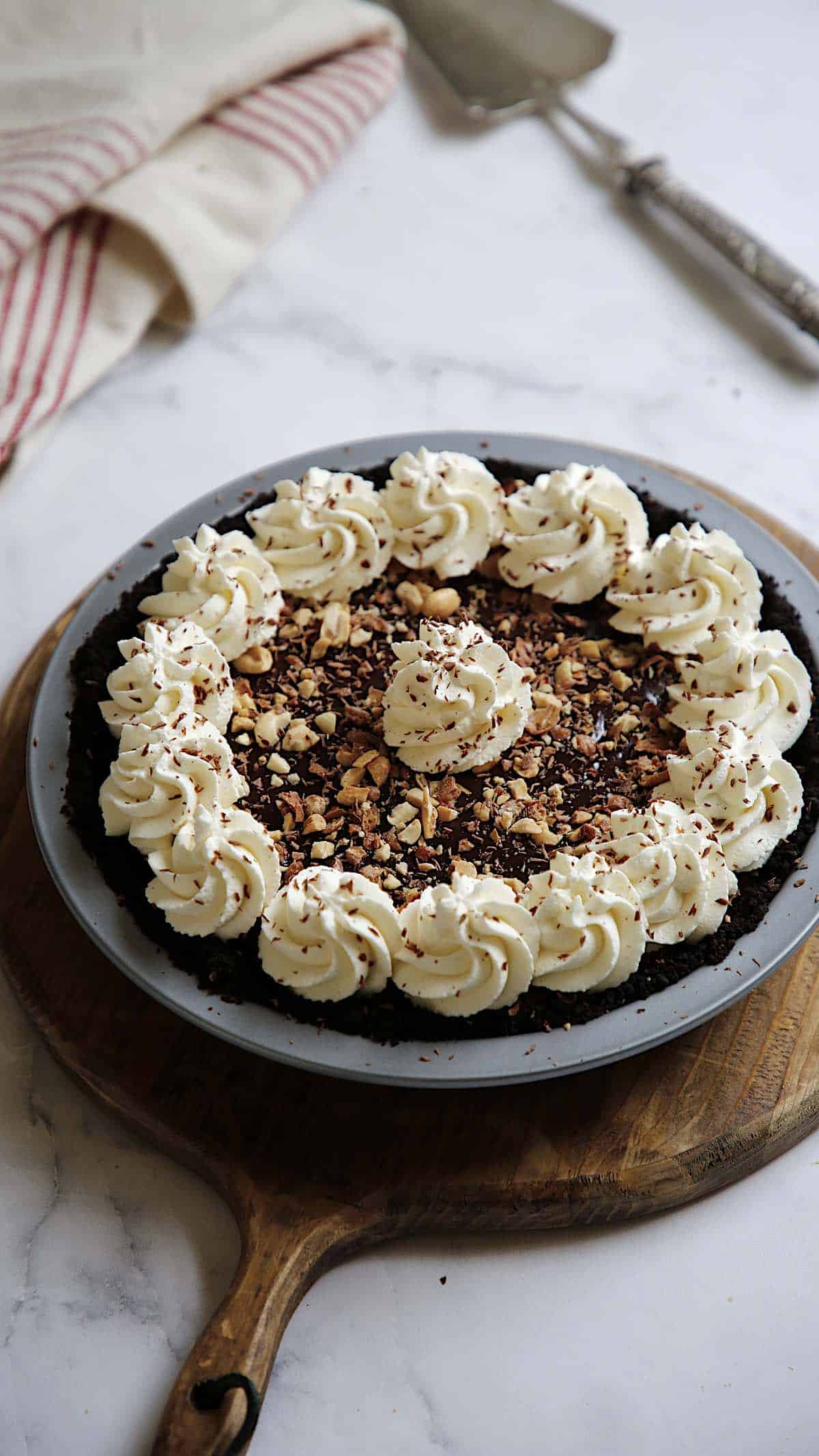 a chocolate peanut butter pie with whipped cream dollops, red dish cloth and pie server