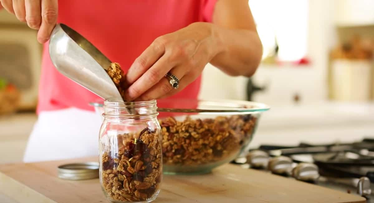 a person filling mason jars with granola with a scoop