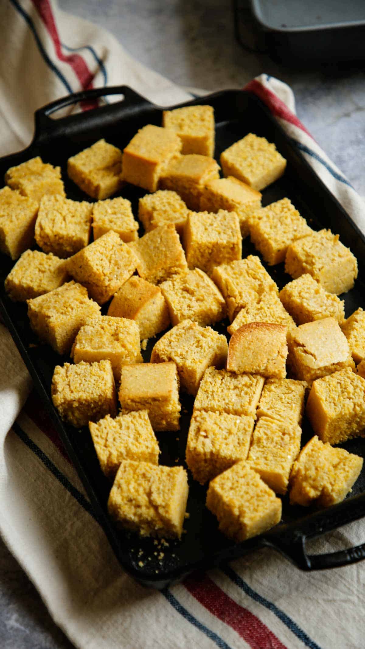 Toasted cubes of cornbread on a cast iron baking pan