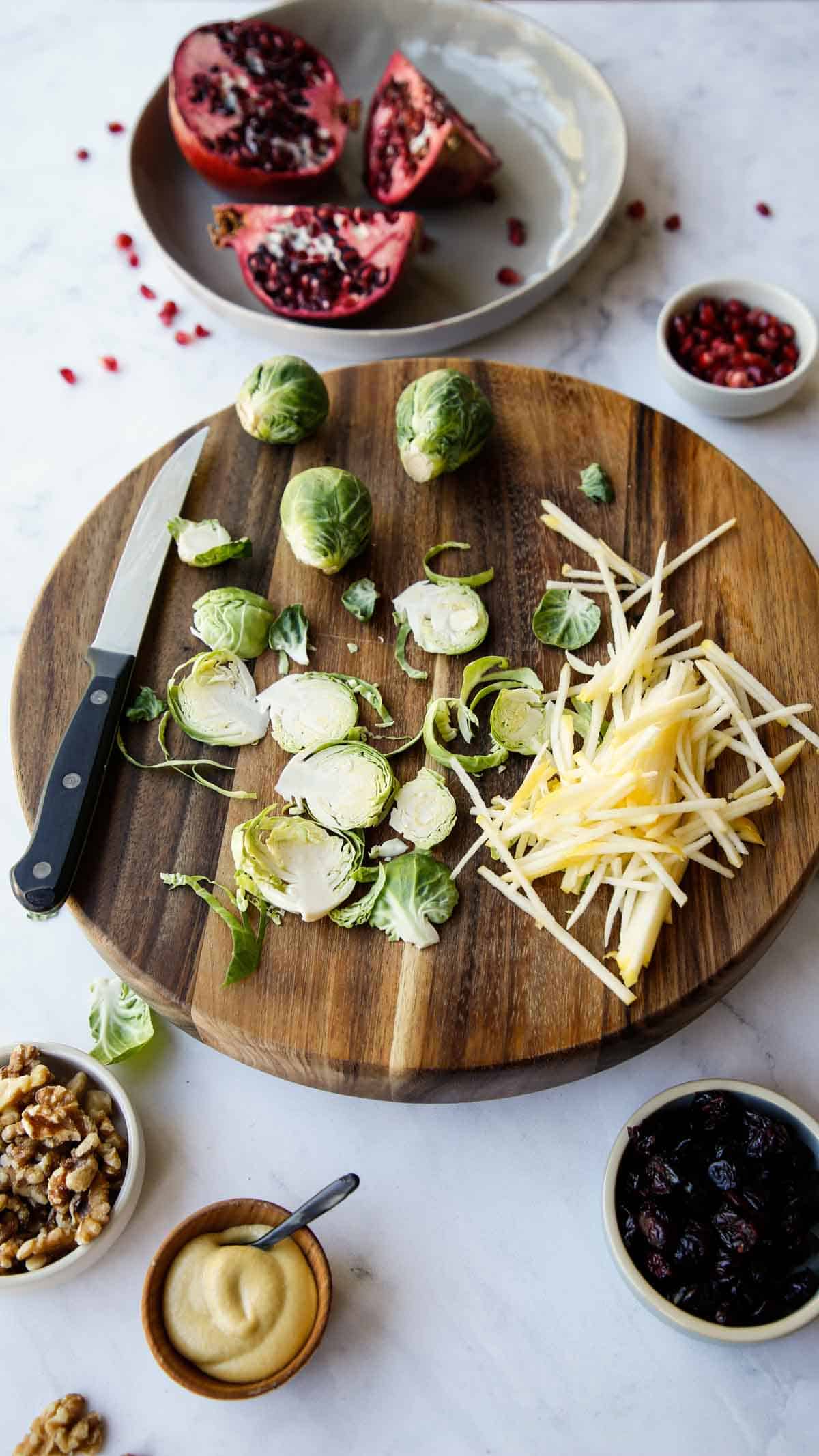 Sliced Brussel Spouts, Apples and Pomegrantes on a board and counter with mustard, nuts and dried cranberries