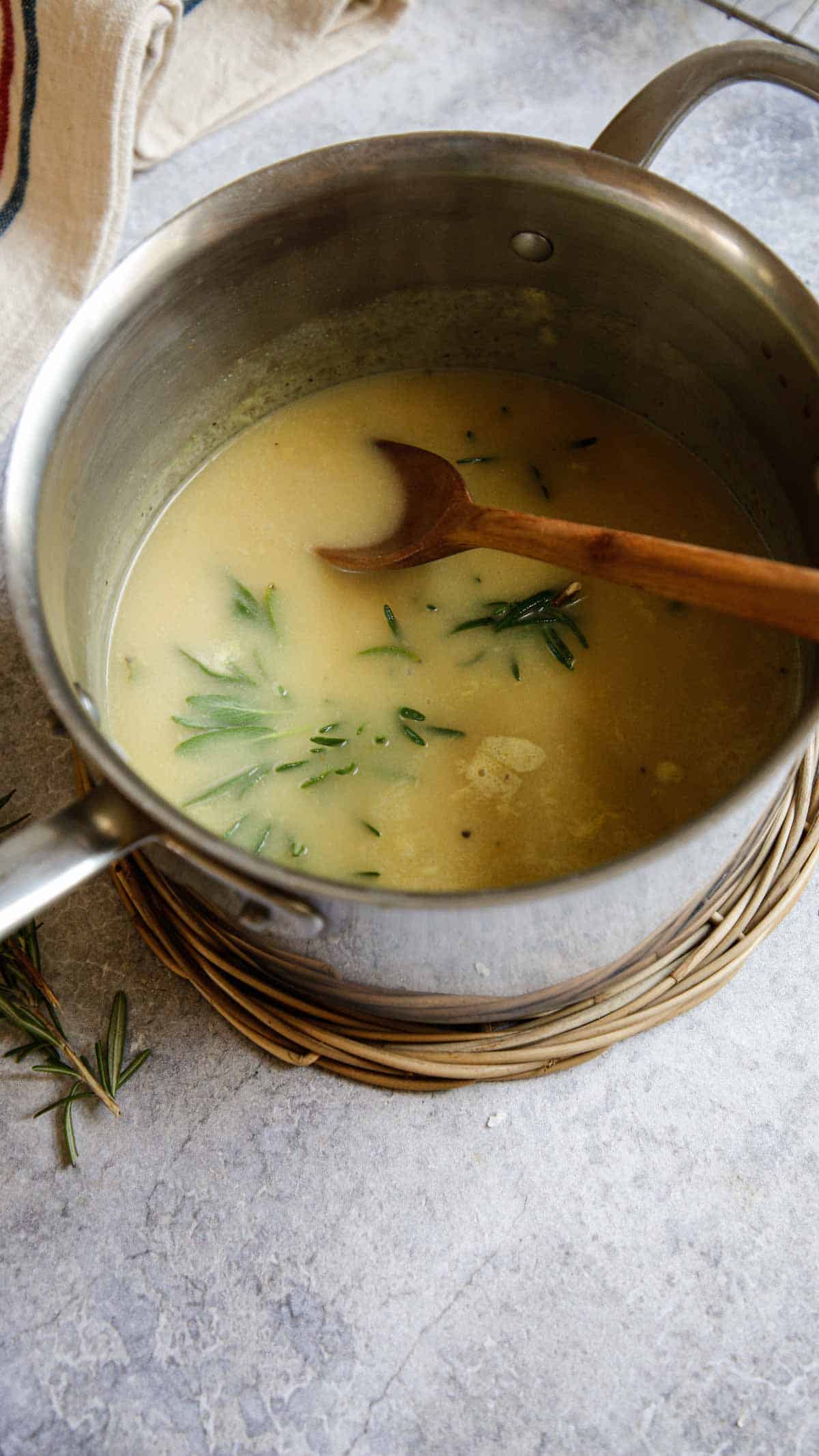 Gravy in pot with herbs steeping and wooden spoon