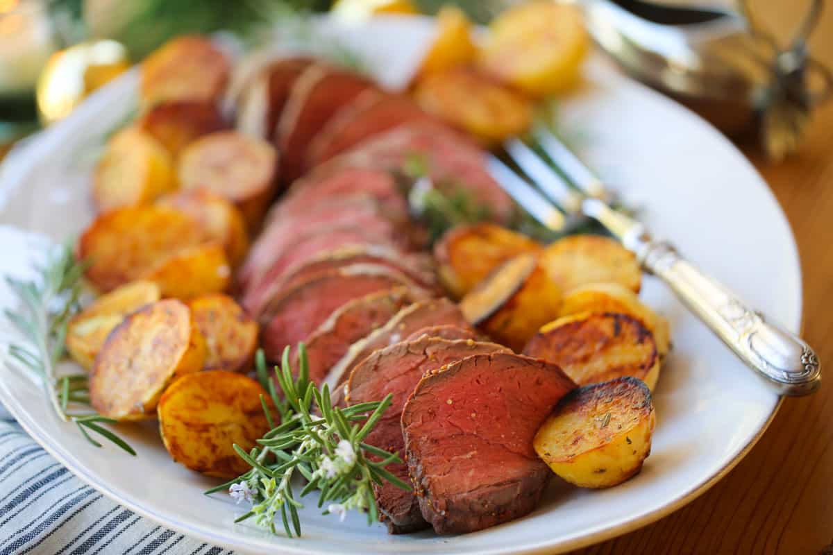 Medium cooked beef, sliced on a platter with roasted potatoes