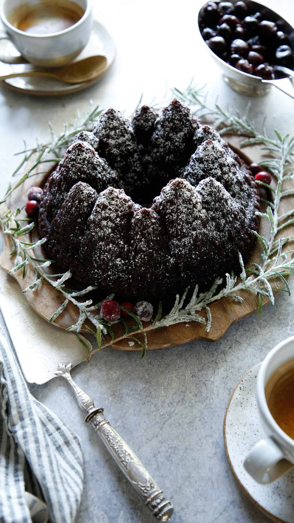 vertical shot of cake decorated with a bowl of cherry sauce coffee cups and silver cake server