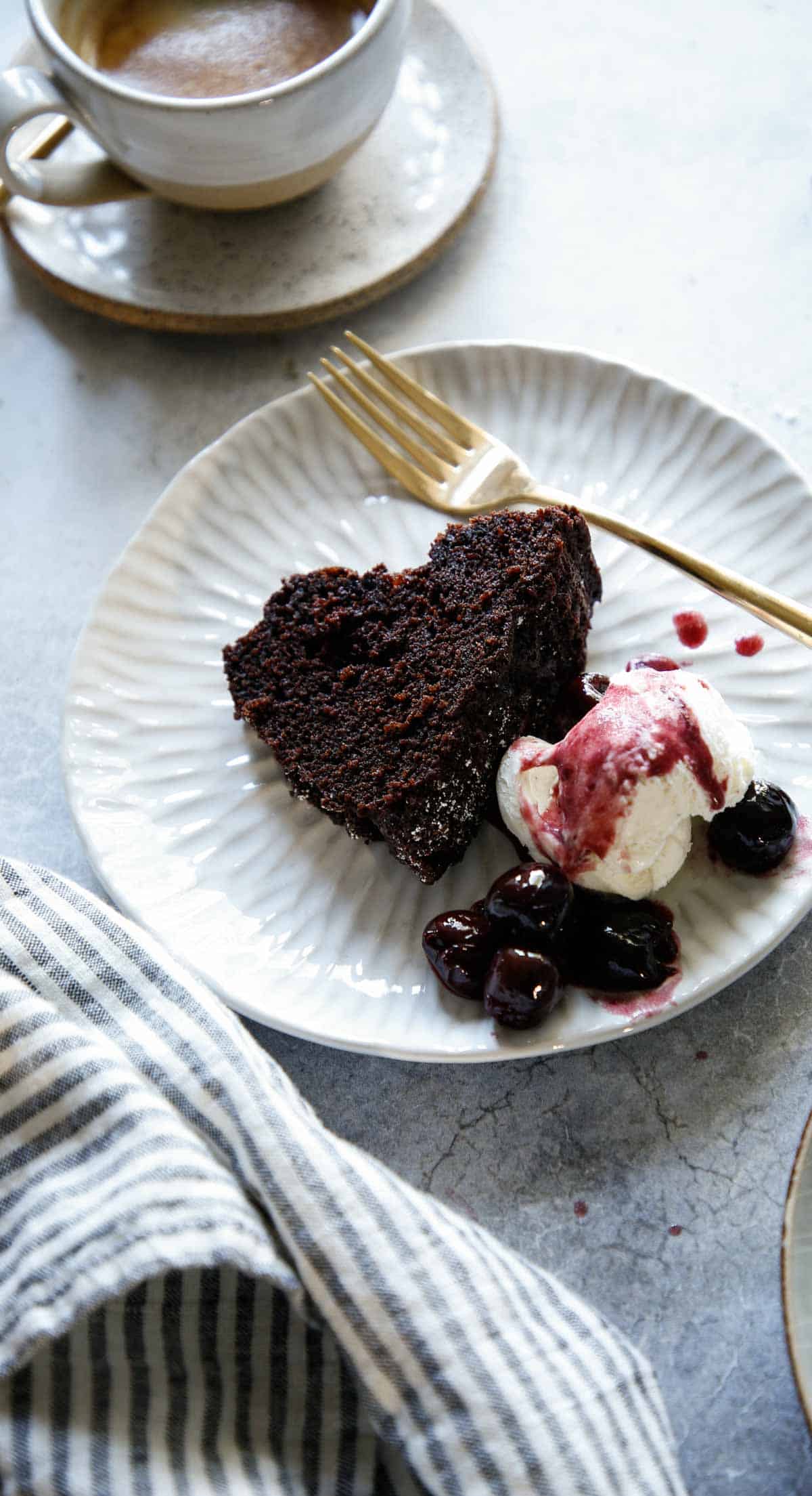 a slice of chocolate cake on a plate with vanilla ice cream and cherry sauce with coffee cup