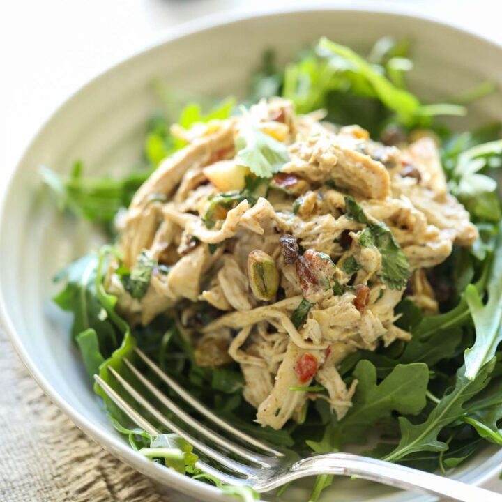 A scoop of chicken salad mixed with yogurt and spices on a bed of greens