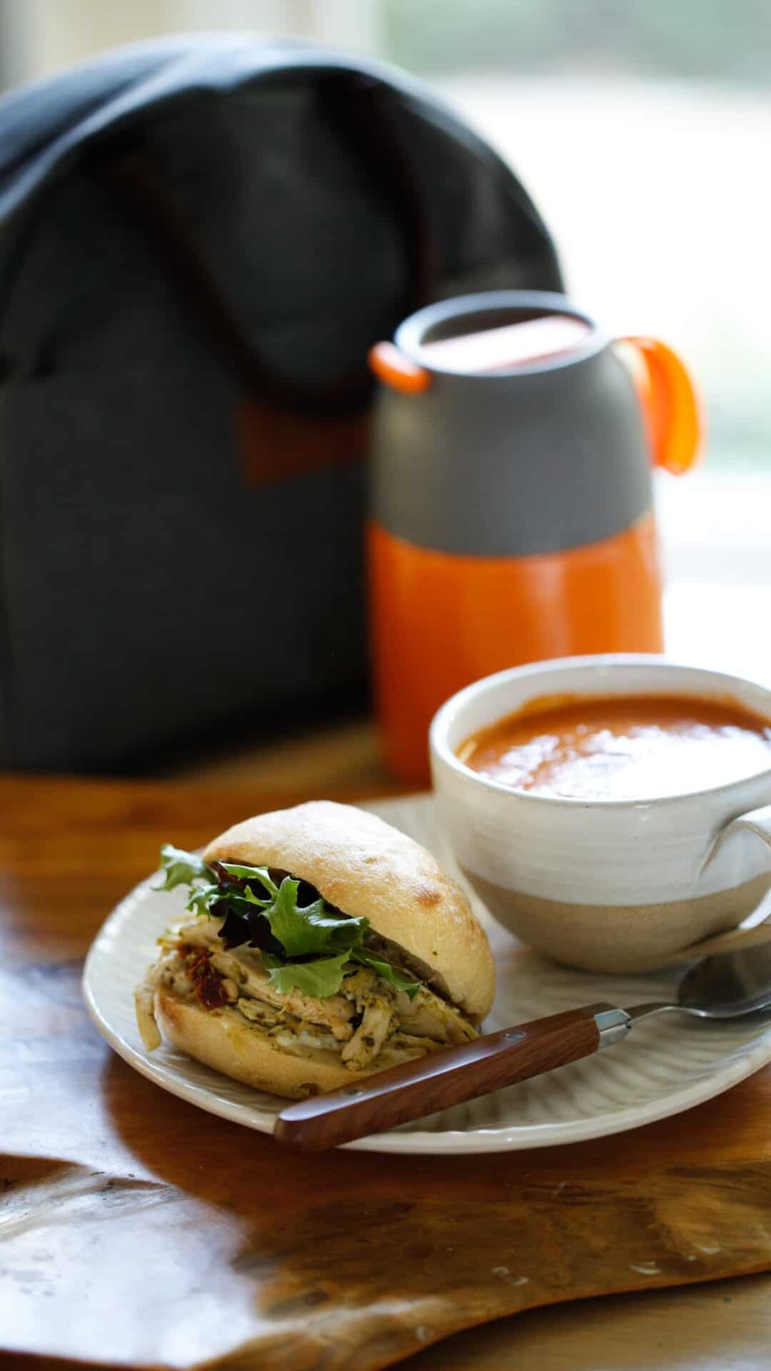 Soup and sandwich on plate with thermos and lunch bag in background