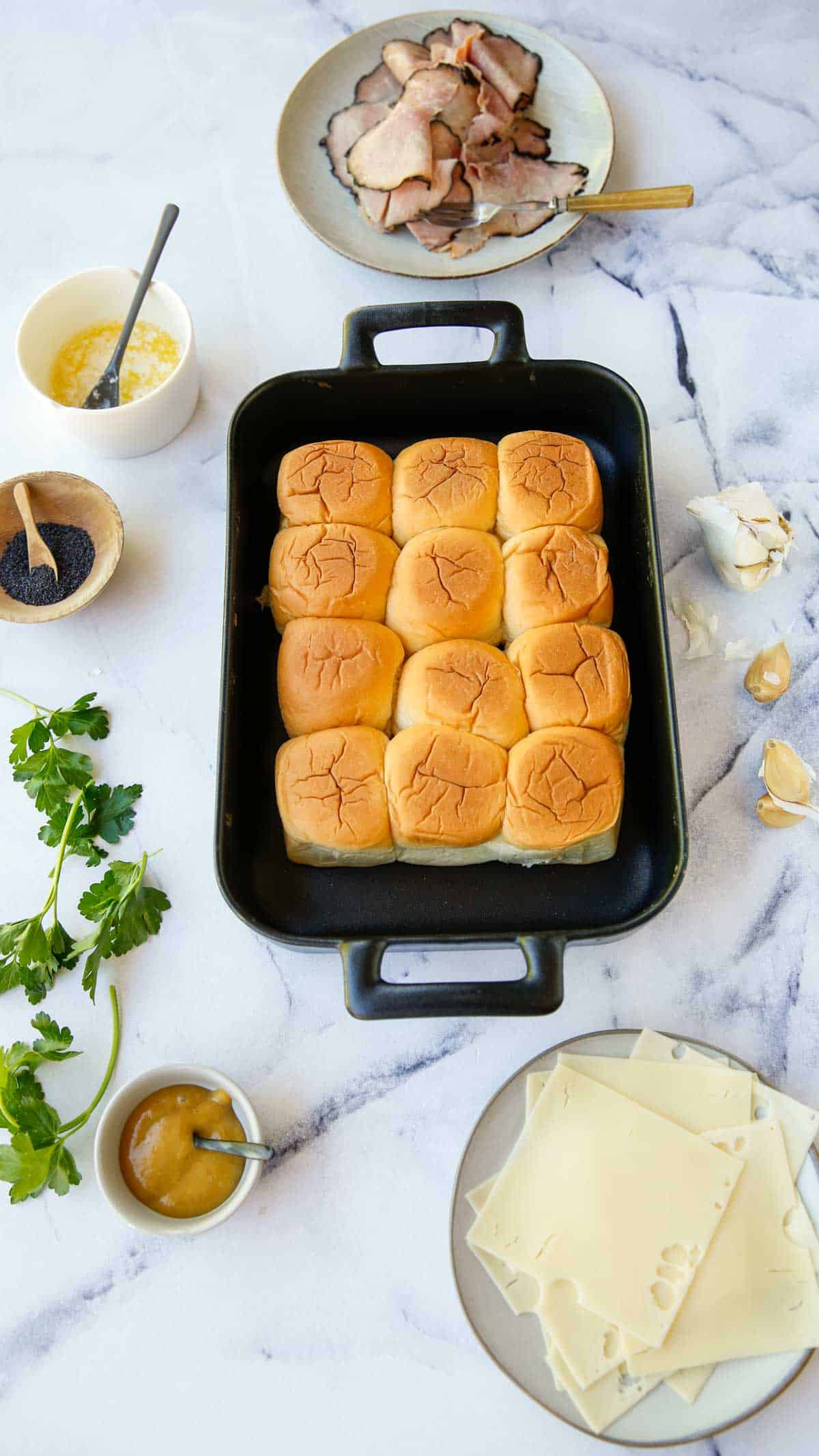 Ingredients for slider recipe laid out on a counter. Includes Hawaiian Rolls, Ham and CHeese, Honey Mustard, Garlic and Parsley