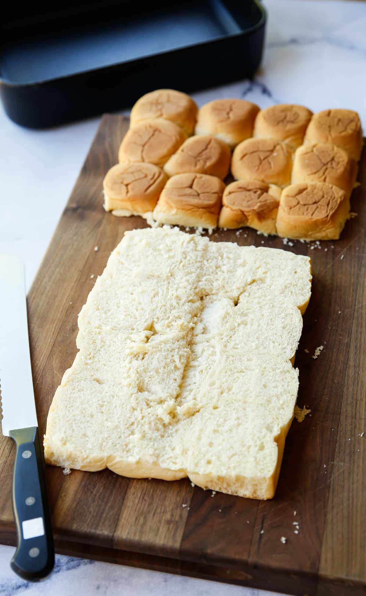 A mass of Hawaiian Sweet Rolls sliced in half, on a cutting board with the top removed