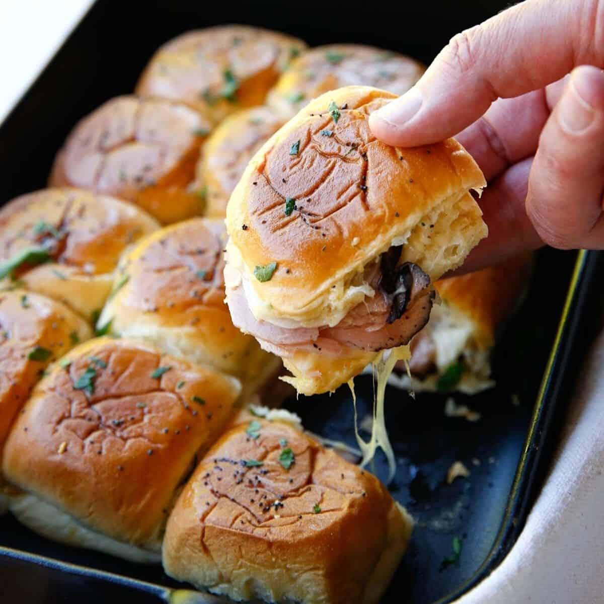 A man picking up a Ham and Cheese Slider from a casserole dish