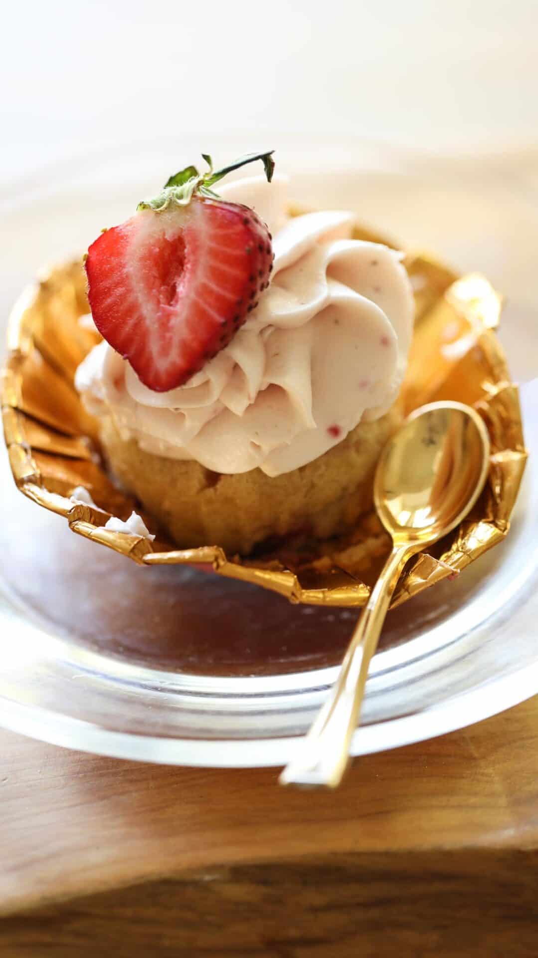 a strawberry cupcake in a gold lined cupcake wrapper opened