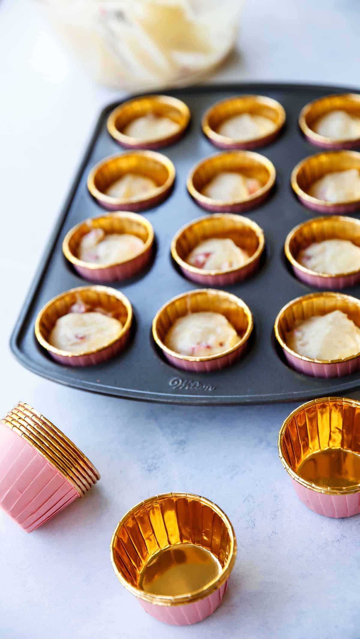 A cupcake tin with cupcake papers filled with strawberry cupcake batter