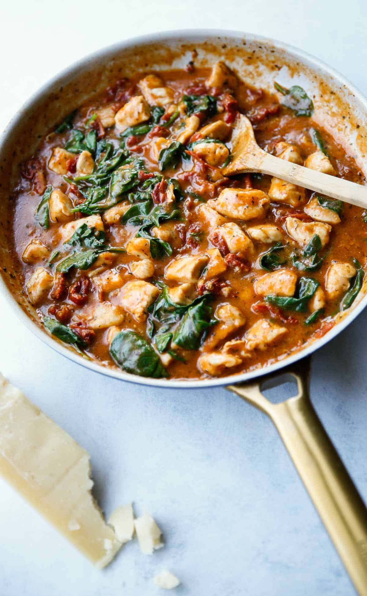 a skillet of creamy Tuscan Chicken with a wedge of parmesan cheese