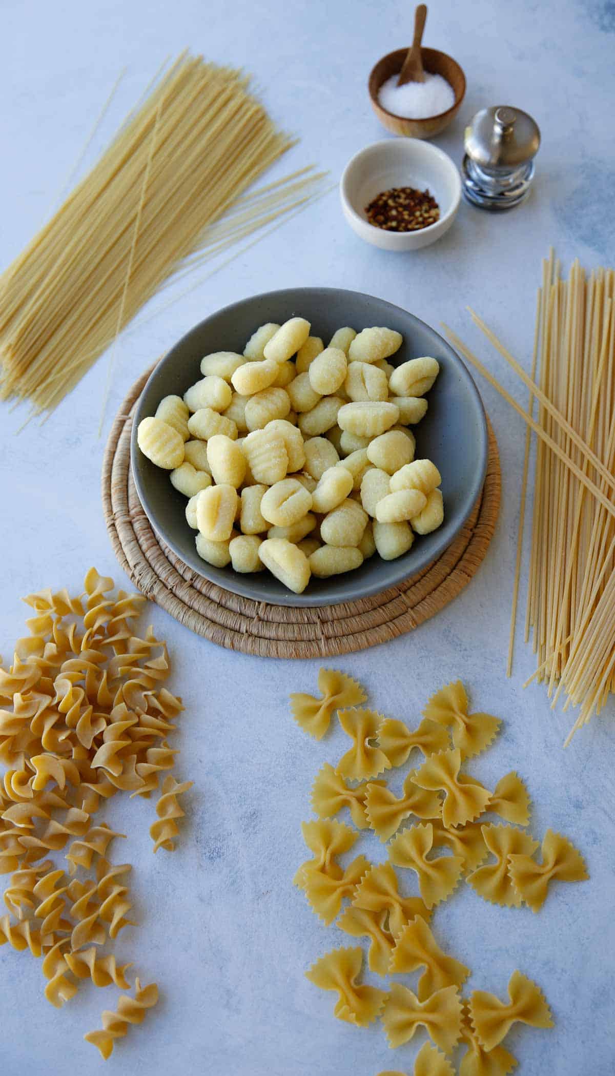 a collection of pasta varieties on a counter including gnocchi, bow-tie, spaghetti and angel hair