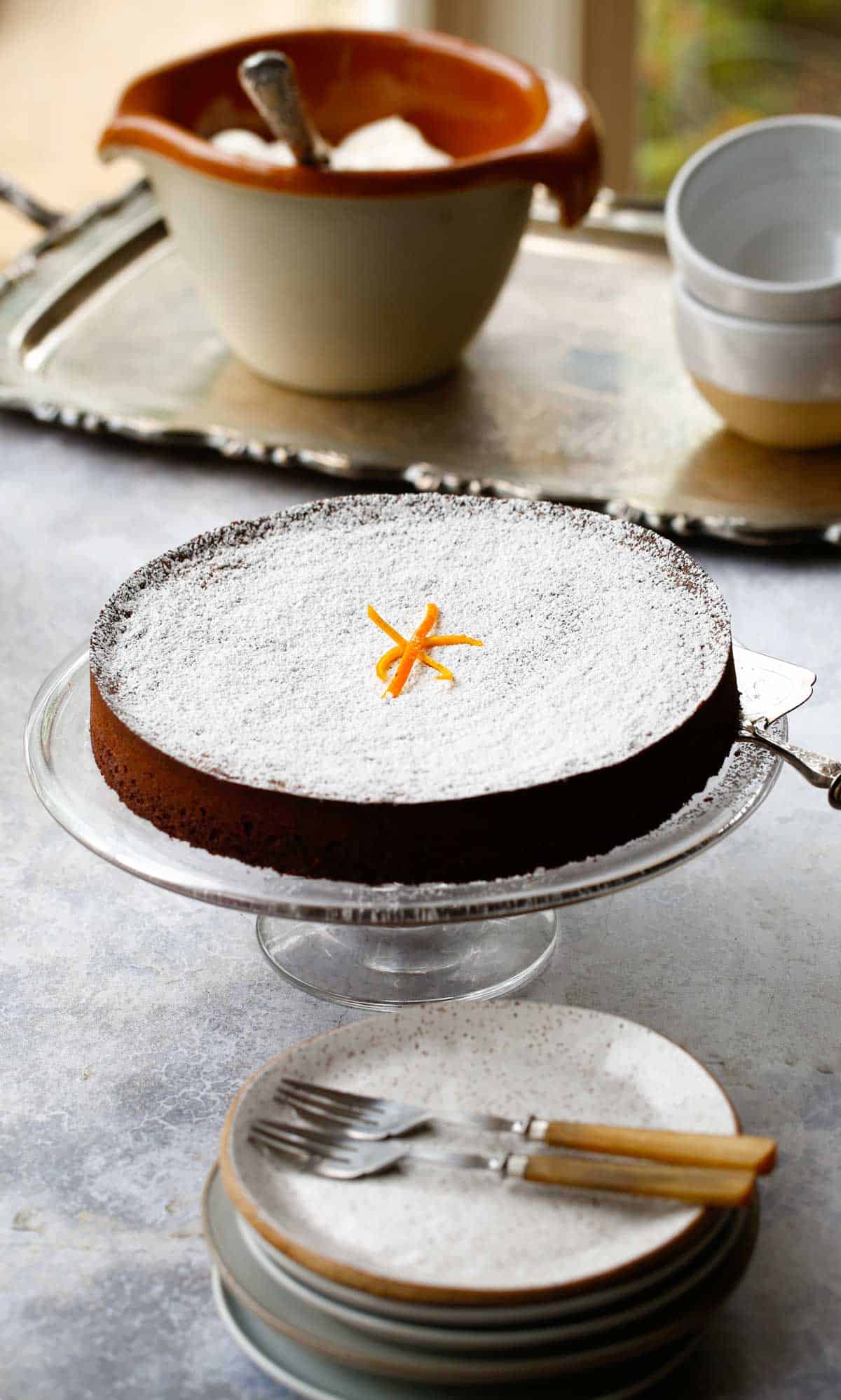 a large cake stand with a whole chocolate cake resting on it dusted with powdered sugar