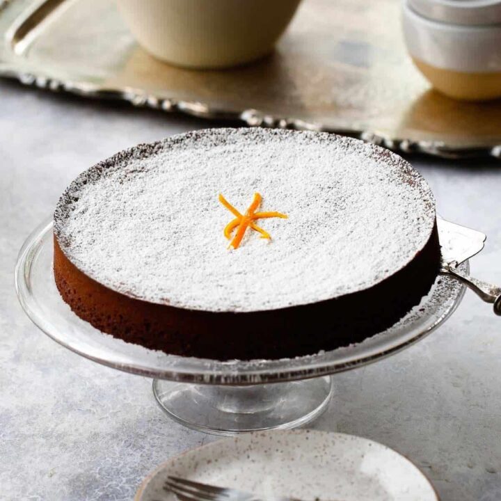 A cake stand with a chocolate cake dusted with Powdered sugar on it