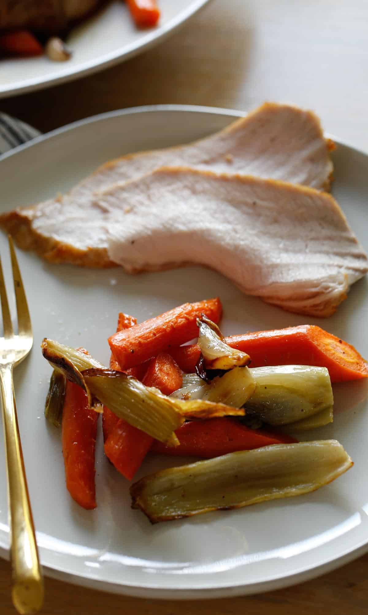 a plate with sliced pork and a side of roasted vegetables with a gold fork