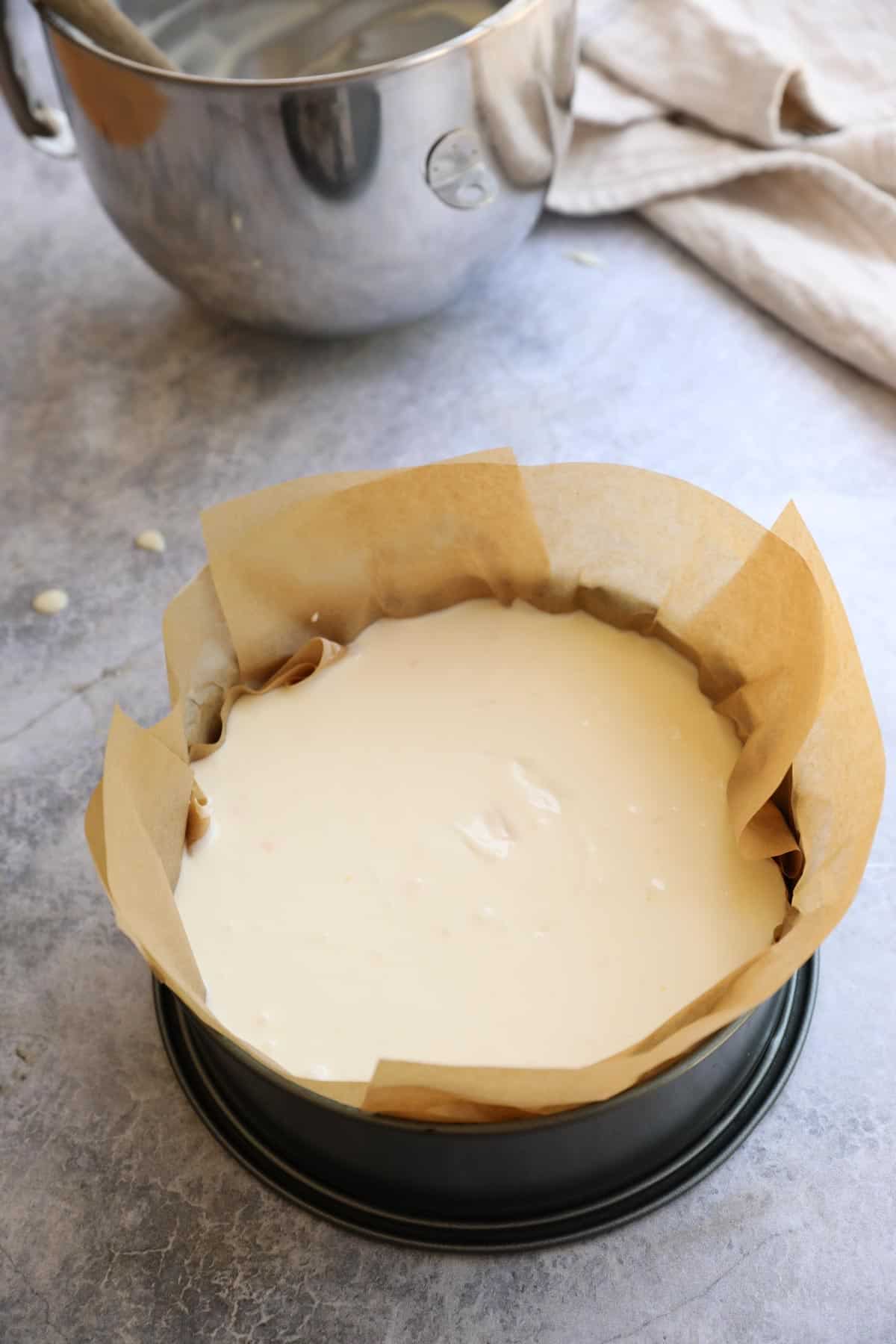 a cheesecake pan lined with parchment paper, filled with batter and a silver mixing bowl