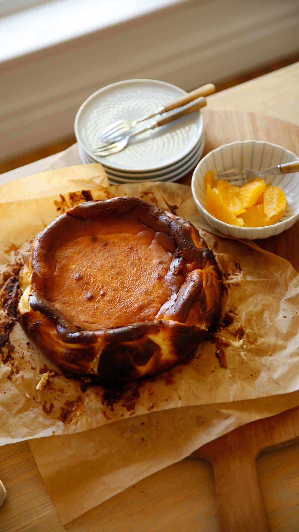 Basque CHeesecake on a board served in parchment paper with orange segments