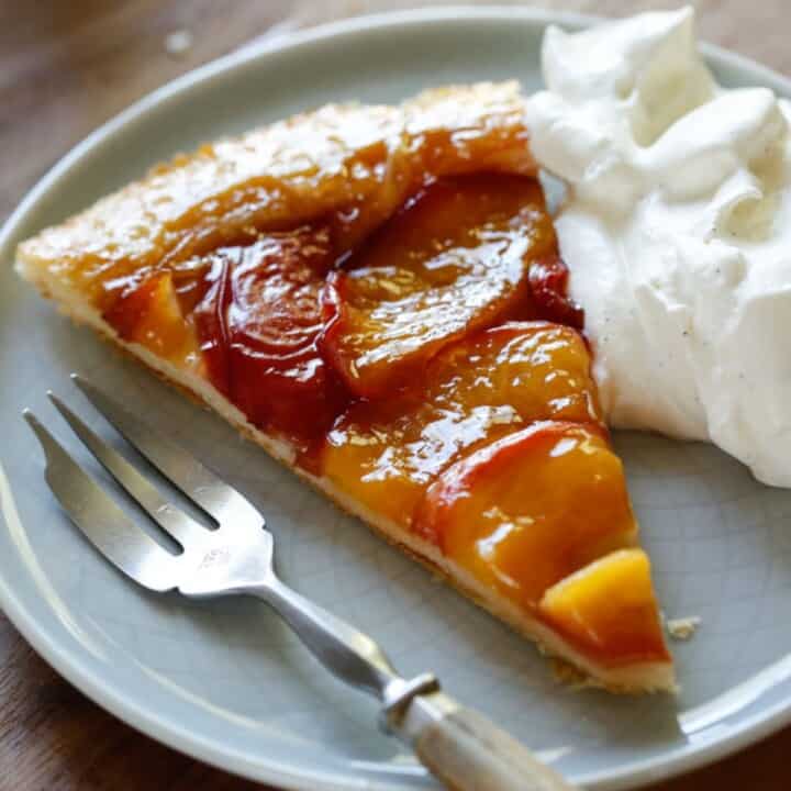 a slice of peach tarte tatin on a plate with whipped cream and fork