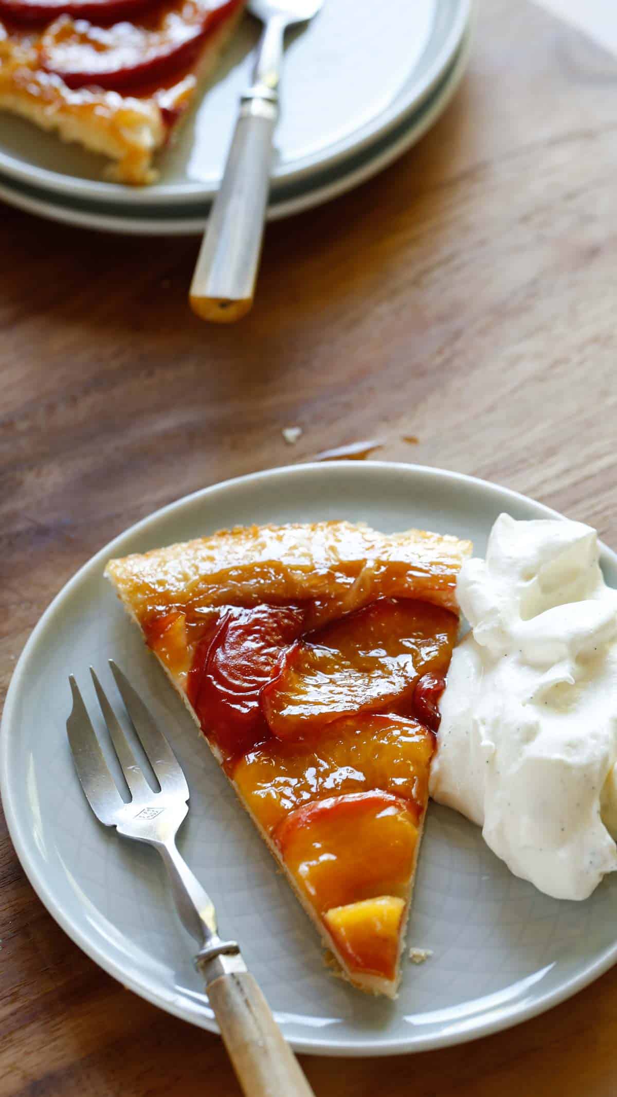 a slice of peach tarte on a plate with whipped cream