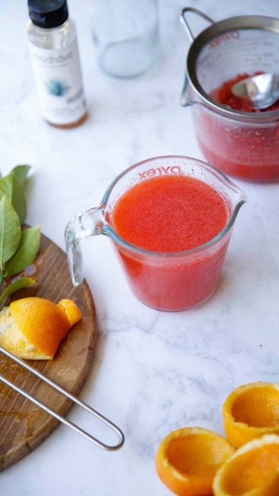 a pyrex pitcher filled with strawberry lemonade with squeezed lemons in the background